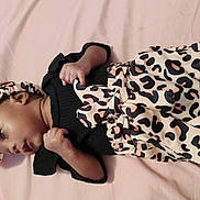 Unique joined the competition — help win amazing prizes! baby, black_top, child, clothing, curious_expression, cute, fabric, head, headband, indoors, infant, leopard_print, lying_down, newborn, pants, person, pink_background, portrait, small_hands, soft_surface