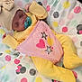 baby, sleeping, pacifier, hat, yellow_clothing, pink_bib, stars, hearts, blanket, polka_dots, cute, infant, cozy, soft, peaceful, child, resting, indoors, colorful, patterned