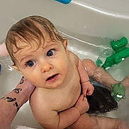 Ellie participe au concours pour gagner de l'argent avec cette photo : baby, bathtub, water, child, toy, green_toy, blue_toy, tattoo, arm, wet_hair, bath, bathroom, towel, skin, person, sitting, looking_up, naked, indoor, cute