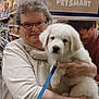 woman, glasses, puppy, dog, pet_store, pet_food, leash, white_dog, smile, holding, indoor, shelf, shopping, store, animal, cute, friendly, fur, happy, person