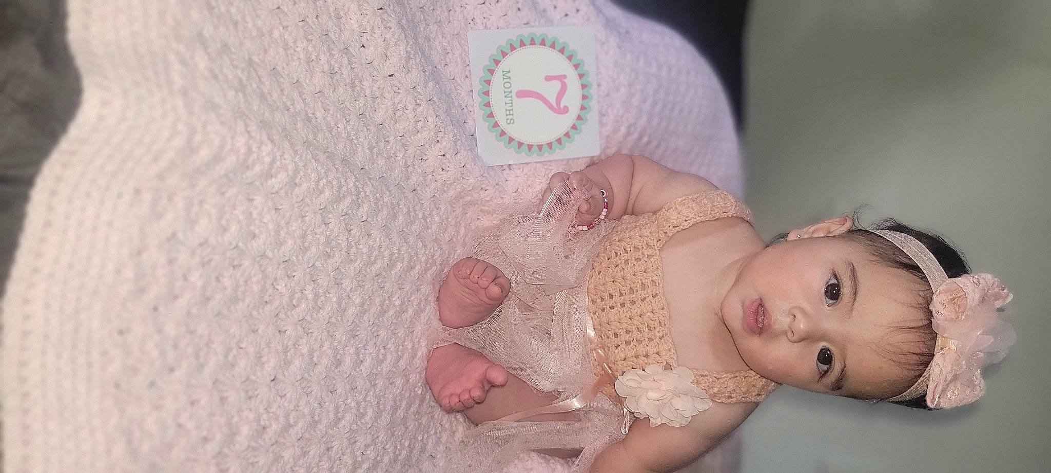 Alannah is registered to the contest to win money with this photo: abdomen, baby, baby_products, baby_toddler_clothing, comfort, dress, embellishment, eyelash, fashion_accessory, hair_accessory, linens, pattern, peach, person, pink, skin, sleeve, textile, toddler, wood