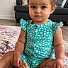 baby, child, infant, sitting, curly_hair, turquoise_outfit, heart_pattern, rug, colorful_rug, living_room, sofa, cushions, clock, wooden_floor, cute, indoors, portrait, looking_at_camera, floor, home