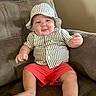 baby, child, infant, hat, striped_clothing, shorts, red_shorts, shirt, striped_shirt, armchair, furniture, smile, happy, cute, indoors, person, plush, relaxed, comfortable, portrait