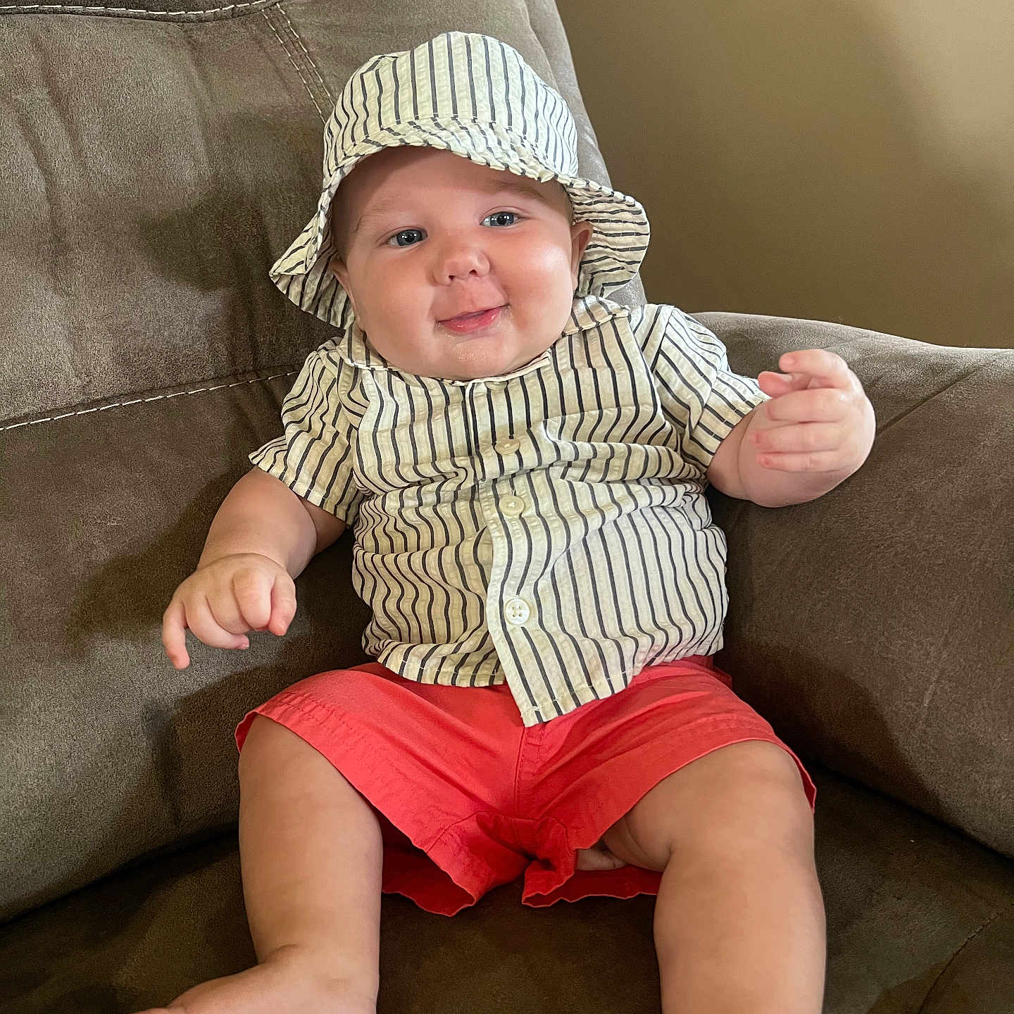Grayson is registered to the contest to win money with this photo: baby, child, infant, hat, striped_clothing, shorts, red_shorts, shirt, striped_shirt, armchair, furniture, smile, happy, cute, indoors, person, plush, relaxed, comfortable, portrait