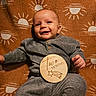 baby, blanket, child, clothing, cozy, cute, face, hand, happy, indoor, infant, knitwear, lying_down, pattern, portrait, smiling, sun, two_months, warm_colors, wooden_sign