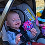 baby, car_seat, child, infant, outdoor, toy, drool, happy, smiling, seatbelt, clothing, plastic, warning_label, sunlight, playful, colorful, fabric, person, portrait, baby_toy