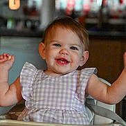 Kelsey joined the competition — help win amazing prizes! toddler, child, smiling, high_chair, dress, purple, checkered, happy, indoor, kitchen, face, arms_raised, baby, person, furniture, seat, cute, young, expression, celebration