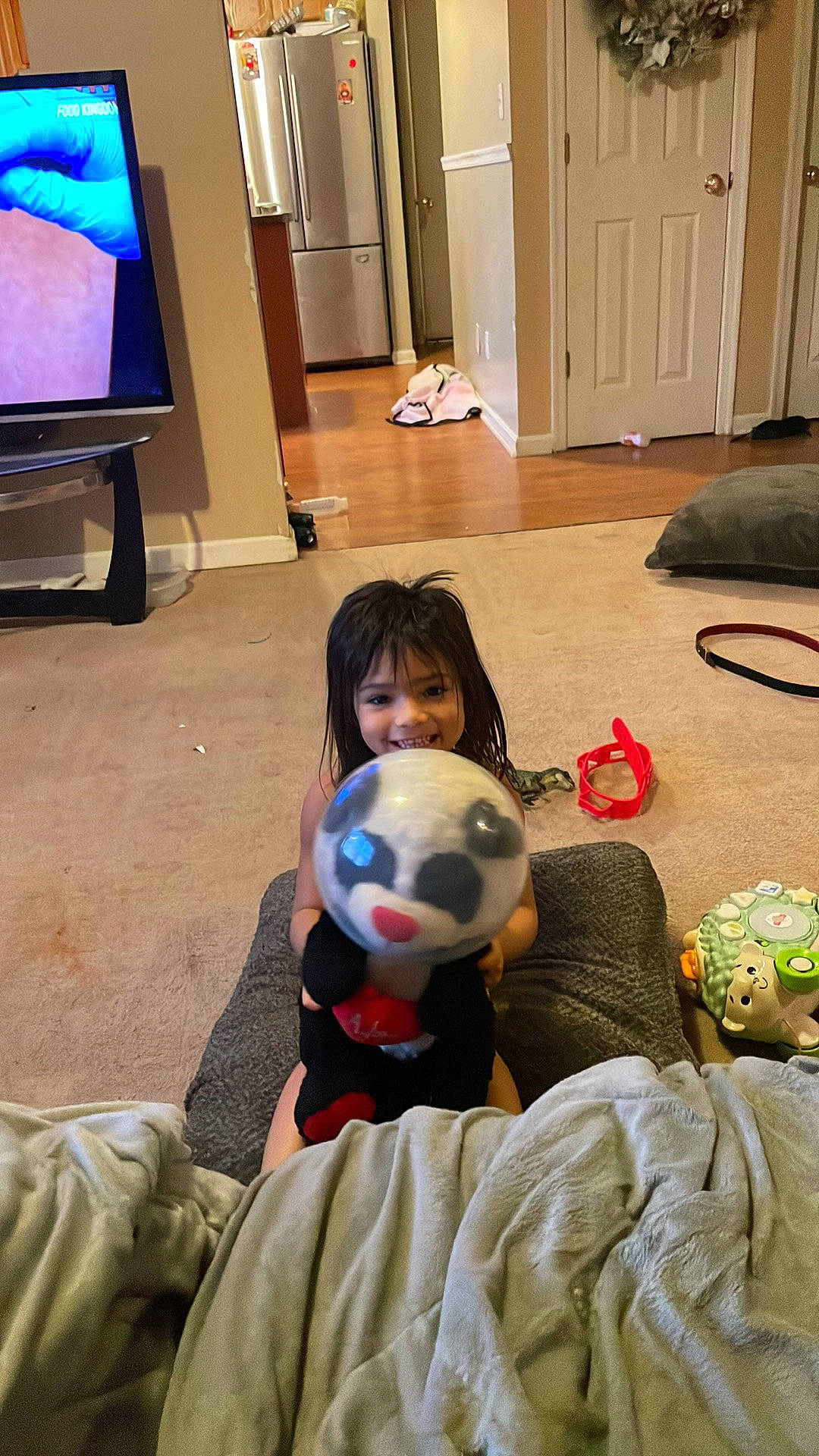 Chloe is registered to the contest to win money with this photo: ball, child, comfort, door, event, floor, flooring, football, fun, hardwood, joy, leisure, luggage_and_bags, person, room, sitting, smile, sports_equipment, stuffed_toy, television