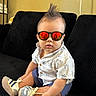 Kaleb is registered to the contest to win money with this photo: baby, child, sunglasses, mohawk, shorts, shirt, sneakers, couch, indoor, fashion, cool, reflection, seated, black_couch, casual, portrait, cute, infant, person, stylish