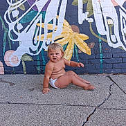 Violette is registered to the contest to win money with this photo: toddler, child, diaper, sidewalk, concrete, brick_wall, mural, colorful_paint, outdoor, barefoot, expression, sitting, playful, young_child, urban, street_art, casual, skin, person, daylight