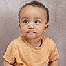 baby, brown_skin, casual_clothing, child, curly_hair, cute, expression, eyes, face, head_and_shoulders, indoor, looking_away, person, portrait, shirt, short_sleeves, soft_background, studio, toddler, young
