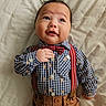 baby, child, infant, boy, clothing, shirt, bow_tie, suspenders, brown_pants, bed, blanket, portrait, cute, smiling, face, hand, lying_down, indoors, fashion, toddler