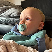 Jayce is registered to the contest to win money with this photo: baby, pacifier, blanket, blue_eyes, close_up, infant, face, portrait, indoor, leather_couch, soft_texture, cozy, child, young, warm, comfort, casual_clothing, head, skin, expression