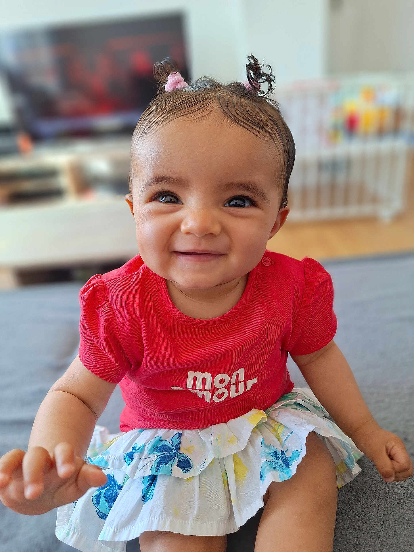 Mélina a rejoint le concours — aidez-le/la à gagner de superbes lots ! baby, child, smiling, red_shirt, skirt, hair_buns, indoor, couch, happy, portrait, person, furniture, living_room, cute, toddler, clothing, sitting, face, skin, expression