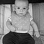 baby, child, infant, bib, clothing, pants, quilt, pattern, face, eyes, sitting, indoors, portrait, black_and_white, expression, cute, young, person, head, hand