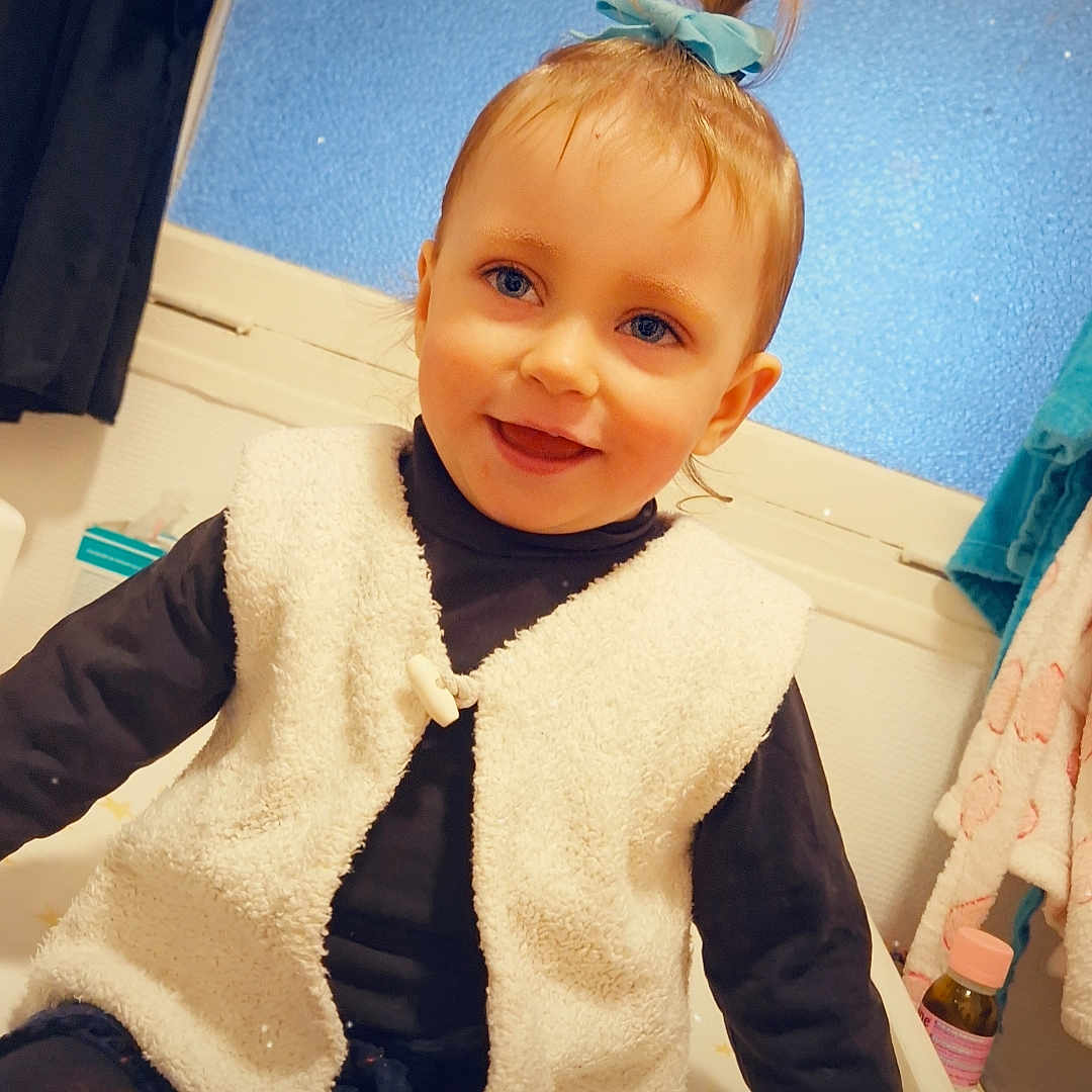 Maya participe au concours pour gagner de l'argent avec cette photo : applique, baby, bodypart, clothing, coat, face, finger, food, furniture, hand, head, knitwear, pants, pattern, person, photography, portrait, sitting, sweater, sweets