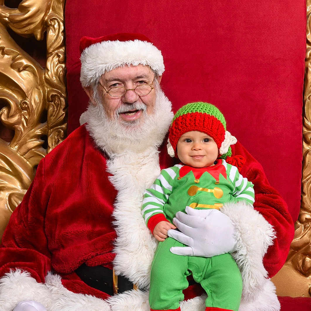 Dorian is registered to the contest to win money with this photo: christmas, christmas_decoration, event, fictional_character, headwear, holiday, joy, lap, person, santa_claus, smile, tradition