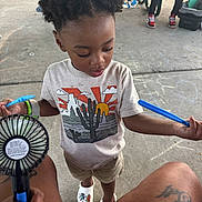 Kashmir is registered to the contest to win money with this photo: child, toddler, hair, tshirt, cactus, crocs, chalk, concrete, fan, legs, person, handheld_fan, outdoor, picnic_table, drawing, shoes, shorts, tattoo, relaxing, summer