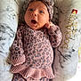 baby, infant, headband, bow, pink_clothing, leopard_print, knitwear, cushion, marble_pattern, surprised_expression, lying_down, indoor, soft_texture, child, newborn, person, cute, cozy, comfortable, portrait