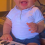 Ilyess a rejoint le concours — aidez-le/la à gagner de superbes lots ! baby, blue_shorts, child, closeup, colorful, cute, drool, face, furniture, hands, happy, indoor, infant, music_toy, person, playing, seat, smiling, toy_keyboard, white_shirt