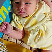 Mia is registered to the contest to win money with this photo: baby, infant, yellow_clothing, lemon_print, blanket, lying_down, curious_expression, cute, newborn, person, skin, hand, head, face, indoors, fabric, soft, close_up, child, portrait