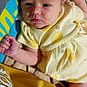 baby, infant, yellow_clothing, lemon_print, blanket, lying_down, curious_expression, cute, newborn, person, skin, hand, head, face, indoors, fabric, soft, close_up, child, portrait