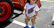 Namari is registered to the contest to win money with this photo: asphalt, blue_shoes, boy, cars, child, curly_hair, machine, outdoor, parking_lot, person, road_marking, shadow, smiling, sunny_day, tan_shorts, toddler, tractor, trees, vehicle, white_tshirt