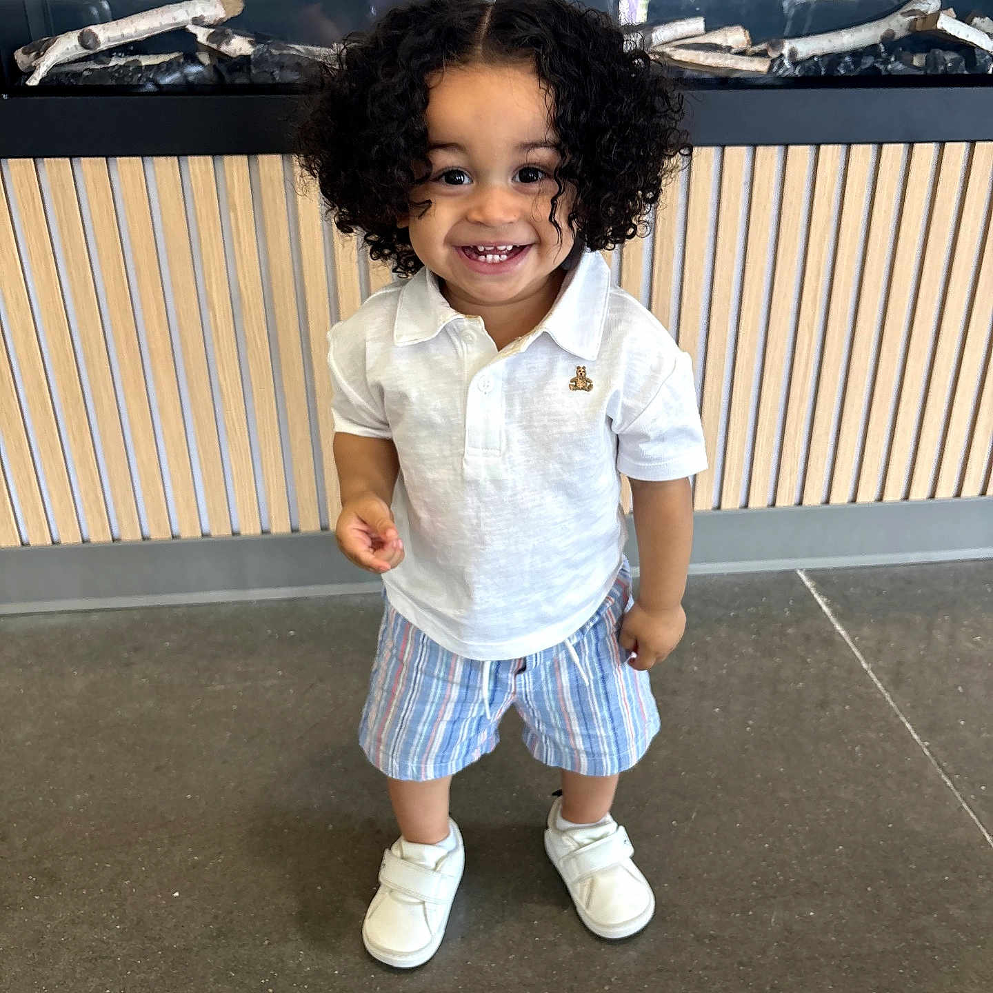 Namari joined the competition — help win amazing prizes! casual_clothing, child, curly_hair, cute, decor, floor, glass_enclosure, happy, indoor, modern, person, playful, reflection, smiling, standing, striped_shorts, toddler, white_polo_shirt, white_shoes, wood_panel