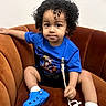 Namari is registered to the contest to win money with this photo: baby_shoes, blue_shirt, blue_shoes, brown_couch, casual_clothing, child, comfortable, couch, curly_hair, cute, holding, indoor, looking_at_camera, pacifier, portrait, sitting, small_child, toddler, white_wall, young_child