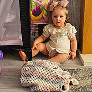 Nyla is registered to the contest to win money with this photo: toddler, child, bow, blanket, crocheted_blanket, floor, indoor, playpen, toy, curious, sitting, clothing, puffed_sleeves, carpet, wood_floor, person, cute, blue_eyes, blonde_hair, home