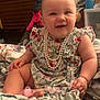 baby, child, smiling, floral_dress, pearl_necklace, bed, blanket, indoor, cute, happy, person, infant, sitting, pacifier, hand, face, skin, head, toy, room