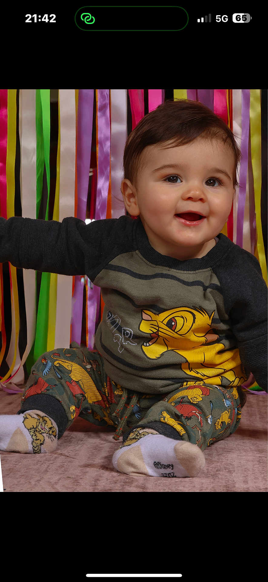 Adrien participe au concours pour gagner de l'argent avec cette photo : baby, child, smiling, sitting, colorful_ribbons, lion_king, clothing, socks, indoor, portrait, happy, cute, young_child, face, hair, background, fabric, playful, person, toddler