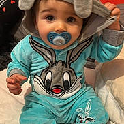Adrien participe au concours pour gagner de l'argent avec cette photo : baby, child, infant, pacifier, hood, onesie, costume, bugs_bunny, cartoon_character, blue_clothing, gray_hood, barefoot, sitting, indoor, soft_texture, cute, face, hands, feet, orange_background