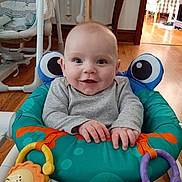 Camden is registered to the contest to win money with this photo: baby, smiling, baby_seat, toy, indoor, child, happy, face, hands, flooring, wooden_floor, playful, infant, clothing, striped_pants, furniture, baby_toys, cozy, room, seat