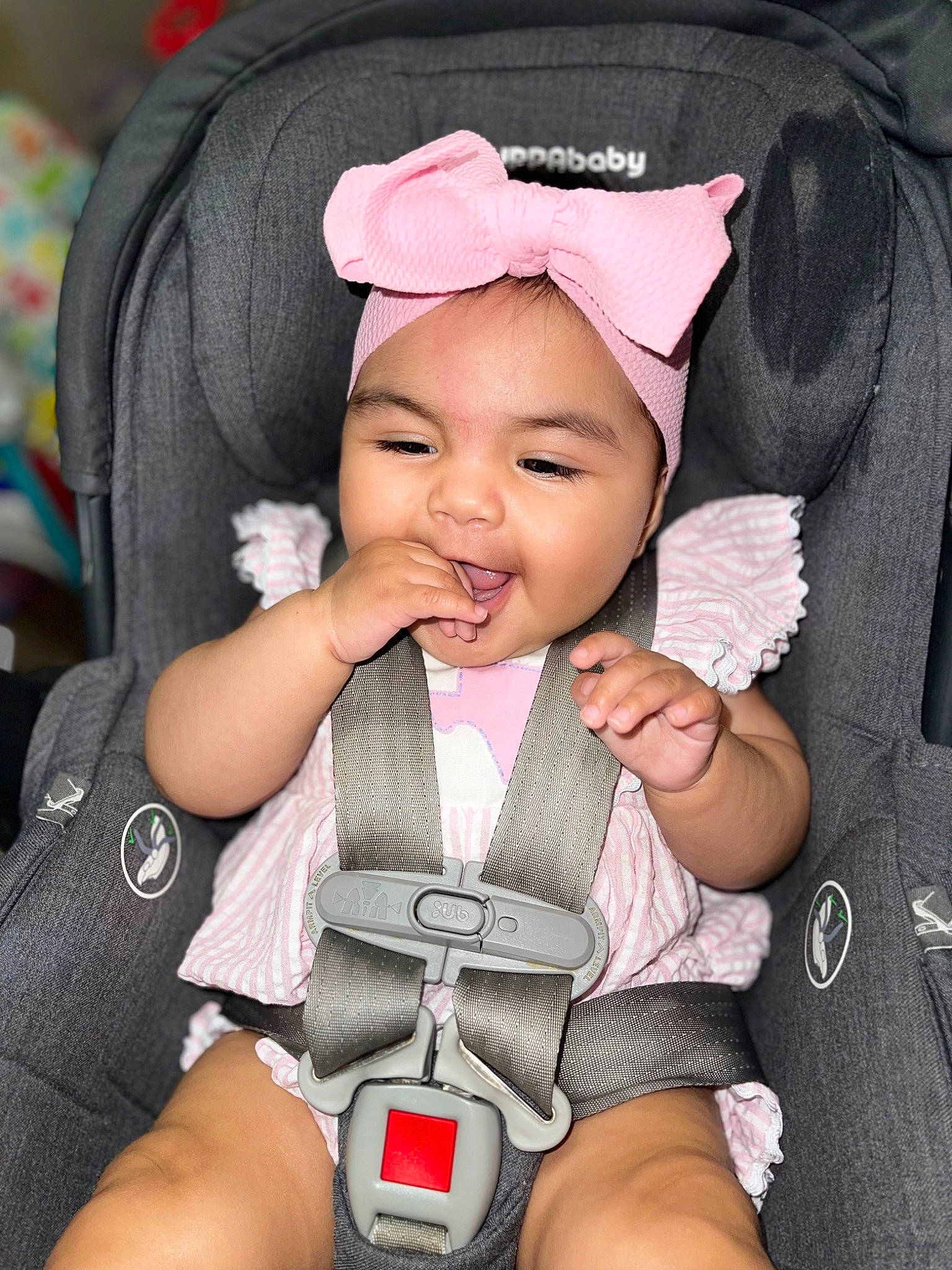Giana is registered to the contest to win money with this photo: baby, baby_in_car_seat, baby_toddler_clothing, cheek, comfort, cool, eye, facial_expression, finger, gesture, hand, headwear, human, organ, outerwear, person, pink, product, seat_belt, skin