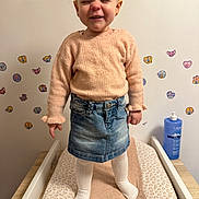 Mayanna participe au concours pour gagner de l'argent avec cette photo : apparel, changing_table, child, cute, denim_skirt, expression, furniture, hair_tied, indoor, person, playful, room, skin_care, smiling, standing, sweater, toddler, wall_stickers, white_tights, young_child