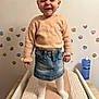 apparel, changing_table, child, cute, denim_skirt, expression, furniture, hair_tied, indoor, person, playful, room, skin_care, smiling, standing, sweater, toddler, wall_stickers, white_tights, young_child