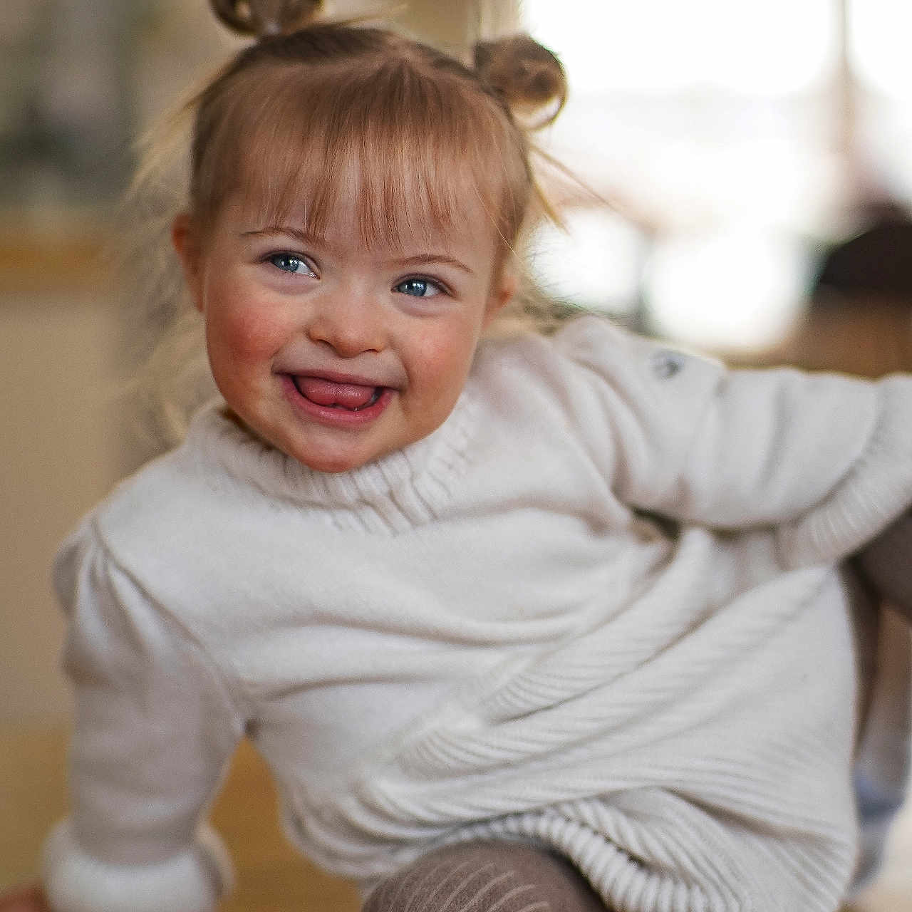 Navah joined the competition — help win amazing prizes! blue_eyes, bokeh, candid, child, cozy, cute, hair_buns, happy, indoor, portrait, real_child, rosy_cheeks, sitting, smile, soft_lighting, sweater, tights, toddler, tongue_out, wooden_floor