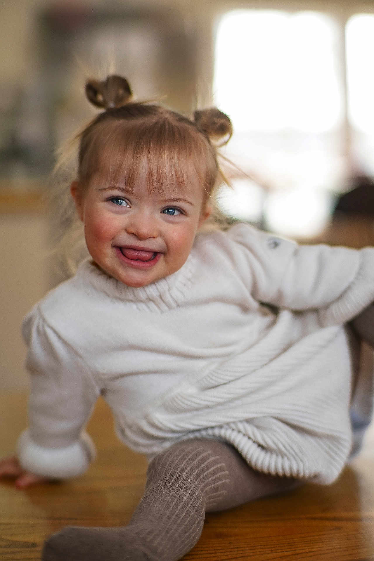 Navah joined the competition — help win amazing prizes! child, toddler, smile, tongue_out, sweater, tights, hair_buns, blue_eyes, rosy_cheeks, indoor, wooden_floor, portrait, candid, happy, cozy, soft_lighting, bokeh, sitting, cute, real_child