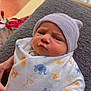 baby, newborn, blanket, beanie, wrapped, indoor, cozy, animal_print, expression, face, person, child, soft_lighting, resting, hand, fabric, cute, portrait, human, infant