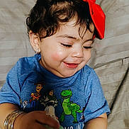 Penelope is registered to the contest to win money with this photo: accessories, baby, baby_bottle, blue_shirt, bracelets, child, clothing, curly_hair, cute, earrings, face, hand, happy, indoor, person, portrait, red_bow, smiling, toddler, toy_story