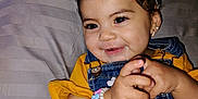 Penelope is registered to the contest to win money with this photo: toddler, child, smiling, headband, bow, denim_overalls, yellow_shirt, bracelet, hands, face, happy, indoor, pillow, water_bottle, earrings, cute, baby, portrait, clothing, expression