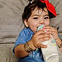Penelope is registered to the contest to win money with this photo: baby_bottle, bed, blue_shirt, bracelets, child, cute, earrings, face, hair, hand, happy, indoors, lying_down, milk, person, pink_nail_polish, portrait, red_bow, smiling, toddler