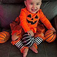 Daniella joined the competition — help win amazing prizes! baby, black_and_white, child, costume, couch, cute, decor, festive, halloween, happy, headband, indoor, leather, orange_clothing, pumpkin, sitting, smiling, striped_socks, toddler, toy