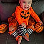 baby, black_and_white, child, costume, couch, cute, decor, festive, halloween, happy, headband, indoor, leather, orange_clothing, pumpkin, sitting, smiling, striped_socks, toddler, toy