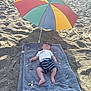baby, beach, umbrella, blanket, sunglasses, sand, rocks, shorts, toddler, relaxing, sunny, child, outdoor, summer, shade, clothing, footwear, person, vacation, leisure