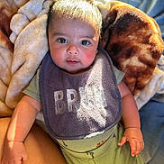 Arlo is registered to the contest to win money with this photo: baby, infant, blanket, bib, clothing, green_pajamas, dinosaur_pattern, face, hand, cute, indoors, portrait, child, person, soft_light, cozy, looking_at_camera, skin, expression, newborn