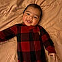 Arlo joined the competition — help win amazing prizes! baby, child, smiling, face, onesie, red, black, checkered, blanket, bed, happy, infant, cute, portrait, person, lying_down, soft, warm, cozy, indoor
