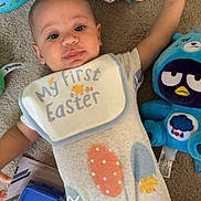 Giovanni is registered to the contest to win money with this photo: baby, child, carpet, plush_toy, blue_bunny, toy_truck, onesie, bib, easter, egg_pattern, indoor, floor, cute, infant, smiling, lying_down, playtime, colorful, young_child, happy