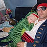 Sawyer is registered to the contest to win money with this photo: child, toddler, sleeping, dinosaur_costume, pirate, pirate_hat, eyepatch, adult, man, costume, portrait, indoor, sitting, lap, cuddling, green, red, blue, sofa, nap
